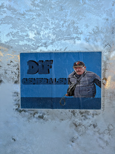 Street sticker A sticker featuring an image of 'Generalen' with the text 'DIF GENERALEN' above the image. 'Generalen' is a man wearing a cap, jacket and a sling bag. The sticker is attached to a window covered in frost.