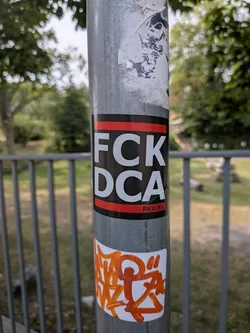 Street sticker A black rectangular sticker featuring red horizontal bars at the top and bottom. Bold white text in the center reads 'FCK DCA', with 'RKU.NU' in small text on the bottom red bar.