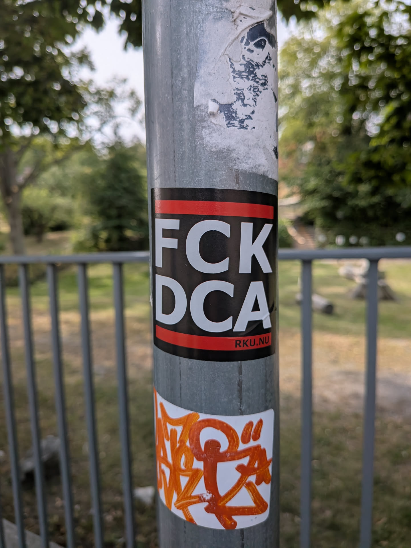 A black rectangular sticker featuring red horizontal bars at the top and bottom. Bold white text in the center reads 'FCK DCA', with 'RKU.NU' in small text on the bottom red bar.