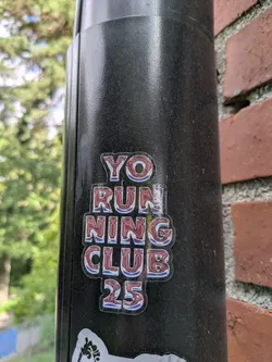 Street sticker The sticker features bold, stylized lettering that reads "YO RUNNING CLUB 25". The letters have a glossy, metallic sheen with a gradient of red and silver, outlined in white and a thin blue border. The overall impression is one of a sporty, modern design.