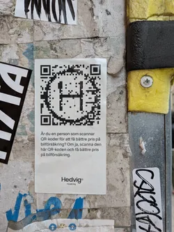 Street sticker A rectangular white sticker pasted on a textured wall. The top half of the sticker features a large black QR code with a stylized letter 'H' integrated into its center. Below the QR code, there is a short paragraph of Swedish text, and at the very bottom, the brand logo 'Hedvig® Försäkring' is printed in a clean, sans-serif font.