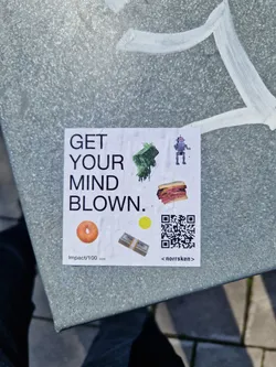 Street sticker A sticker featuring the text 'GET YOUR MIND BLOWN.', along with illustrations of a robot, a sandwich, a bagel, a stack of money, and a QR code. The sticker also includes the text 'Impact/100' and '<norrskn>'.