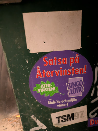 Street sticker The sticker is circular with a purple background and red text that reads "Satsa på Återvinsten!", which encourages recycling. The sticker also shows the text "Både du och miljön vinner!" and the words "Bingo lotto". An oak leaf shape with the words "ÅTER-VINSTEN!"