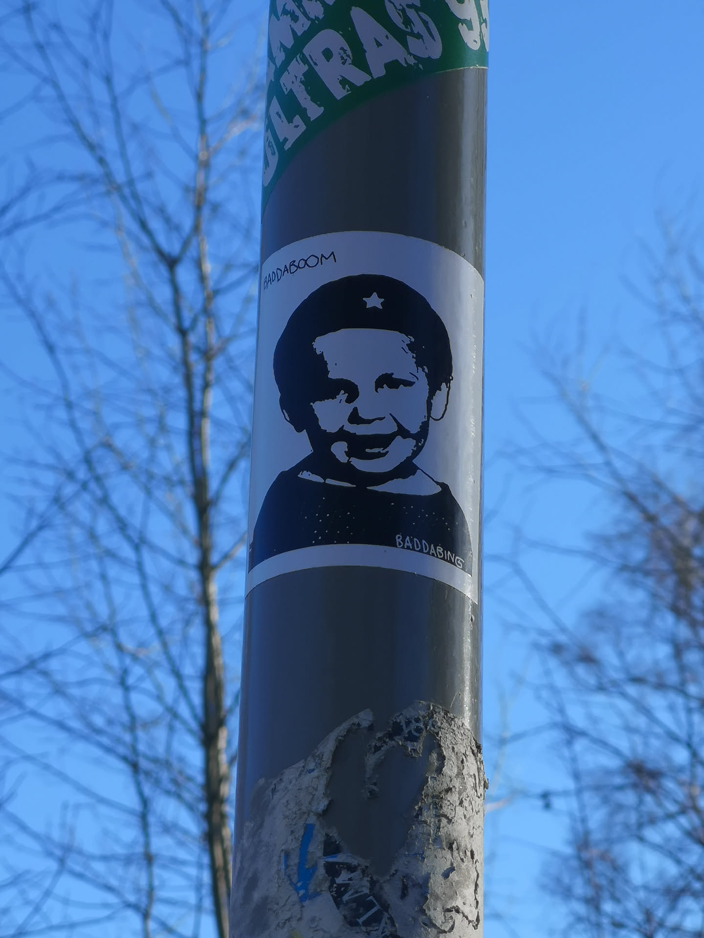 A rectangular, white sticker featuring a high-contrast black and white graphic of a smiling baby's head and shoulders. The baby has a wide grin and is wearing a dark cap adorned with a prominent white five-pointed star on the front. Above the baby's head, the word 'BADDABOOM' is written in a stylized, slightly distressed font. Below the baby's shoulders, the word 'BADDABING' is written in a similar font. The overall style is reminiscent of stencil art or a simplified graphic design.