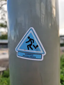 A sticker with a warning sign and the text 'WARNING! WICKED OWNER'. The sign depicts a figure tripping and falling.