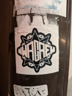 Street sticker Black and white sticker with NWACREW logo. It's a star-shape design with text 'NWACREW' in the center and 'KASE' and 'DUBS' at the bottom.  The numbers 'BS' and '20' are visible on the top left and top right corners respectively. The sticker shows some signs of wear.