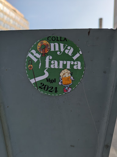 Street sticker A round sticker with green background features a wreath, a walking stick, and a beer mug character. It mentions Colla Ronyai Farra MGD 2024.