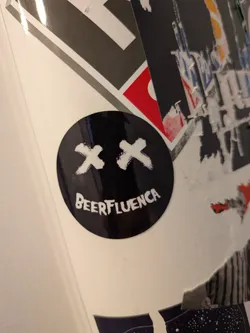 Street sticker A glossy, round black sticker featuring a white graphic of two 'X's for eyes and the text 'BEERFLUENCA' curved to form a smiling mouth.