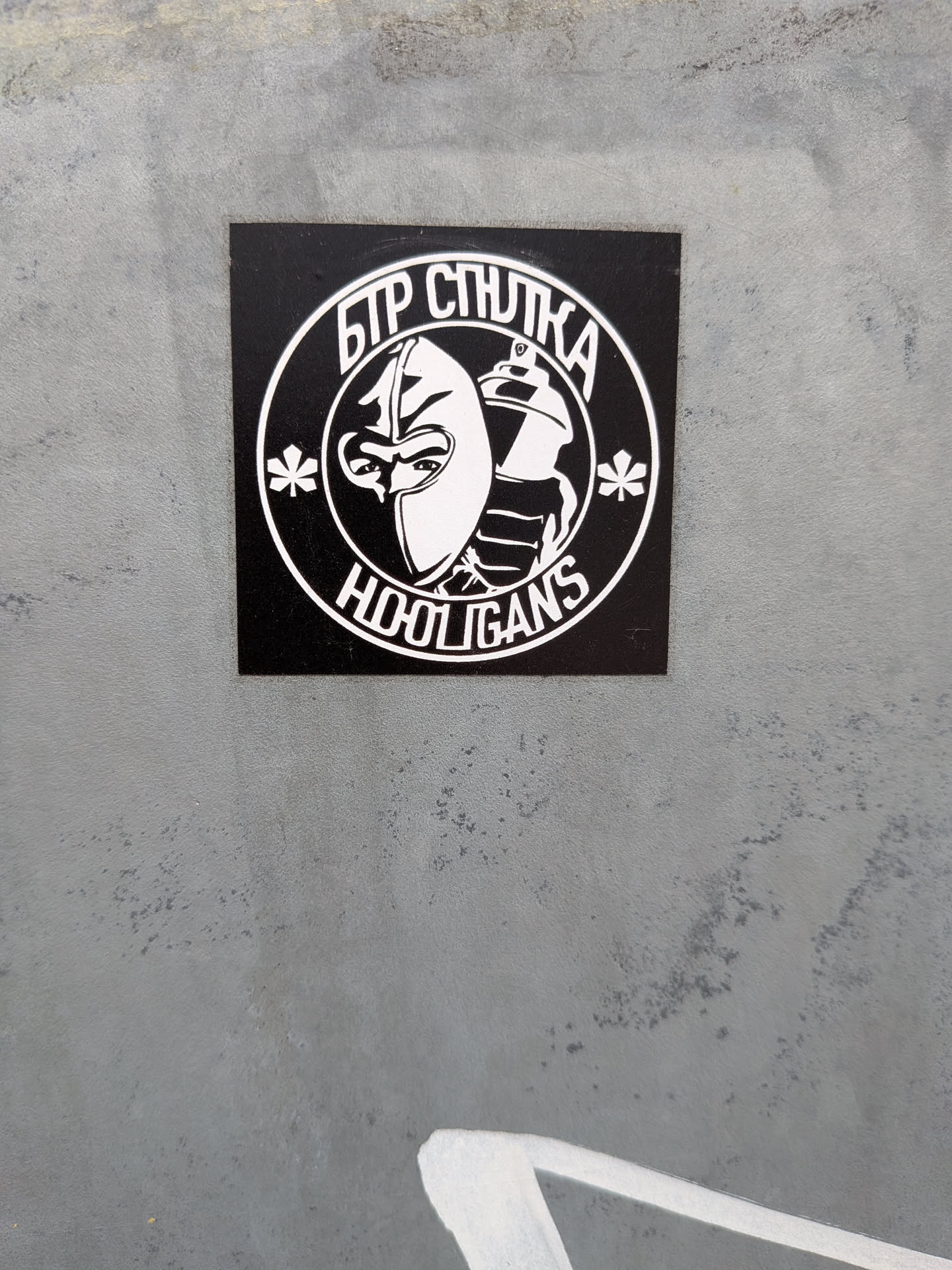 A square black sticker with a white circular emblem. The emblem depicts a character in a balaclava alongside a spray paint can, flanked by two stylized chestnut leaves. Cyrillic text is arched at the top, and 'HOOLIGANS' is written at the bottom.