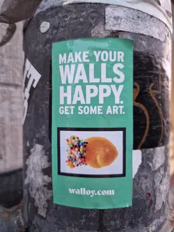 Street sticker A teal and white sticker with the text 'Make Your Walls Happy. Get Some Art.' and a picture of a pastry with sprinkles. The website walloy.com is also visible at the bottom.