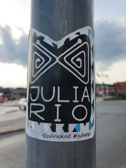 Black and white sticker with a geometric design and the name JULIA RIO written in a stylized font. The sticker also includes a social media handle and hashtag.