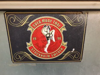 A sticker featuring a Muay Thai fighter in action. The design incorporates the text 'SVEA MUAY THAI', '19', '96', 'STOCKHOLM SWEDEN' and decorative elements. The color scheme is predominantly red, black and gold.