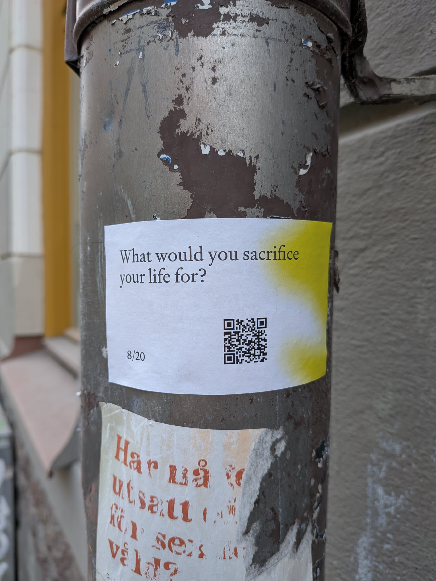 A rectangular sticker with a predominantly white background, featuring a bold, black question 'What would you sacrifice your life for?' in a sans-serif font. To the right of the text, there's a soft, vertical gradient of bright yellow or lime green, fading into the white background. Below the main question, on the left, is the numerical text '8/20', and on the right, a black and white QR code is prominently displayed. The sticker appears slightly curled at the edges, indicating it's adhered to a weathered, dark brown and silver painted metal pole.