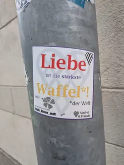 Street sticker White square sticker with a purple border. Features red, purple, and yellow text reading 'Liebe ist die stärkste Waffel*!' alongside heart-shaped waffle illustrations and social handles.