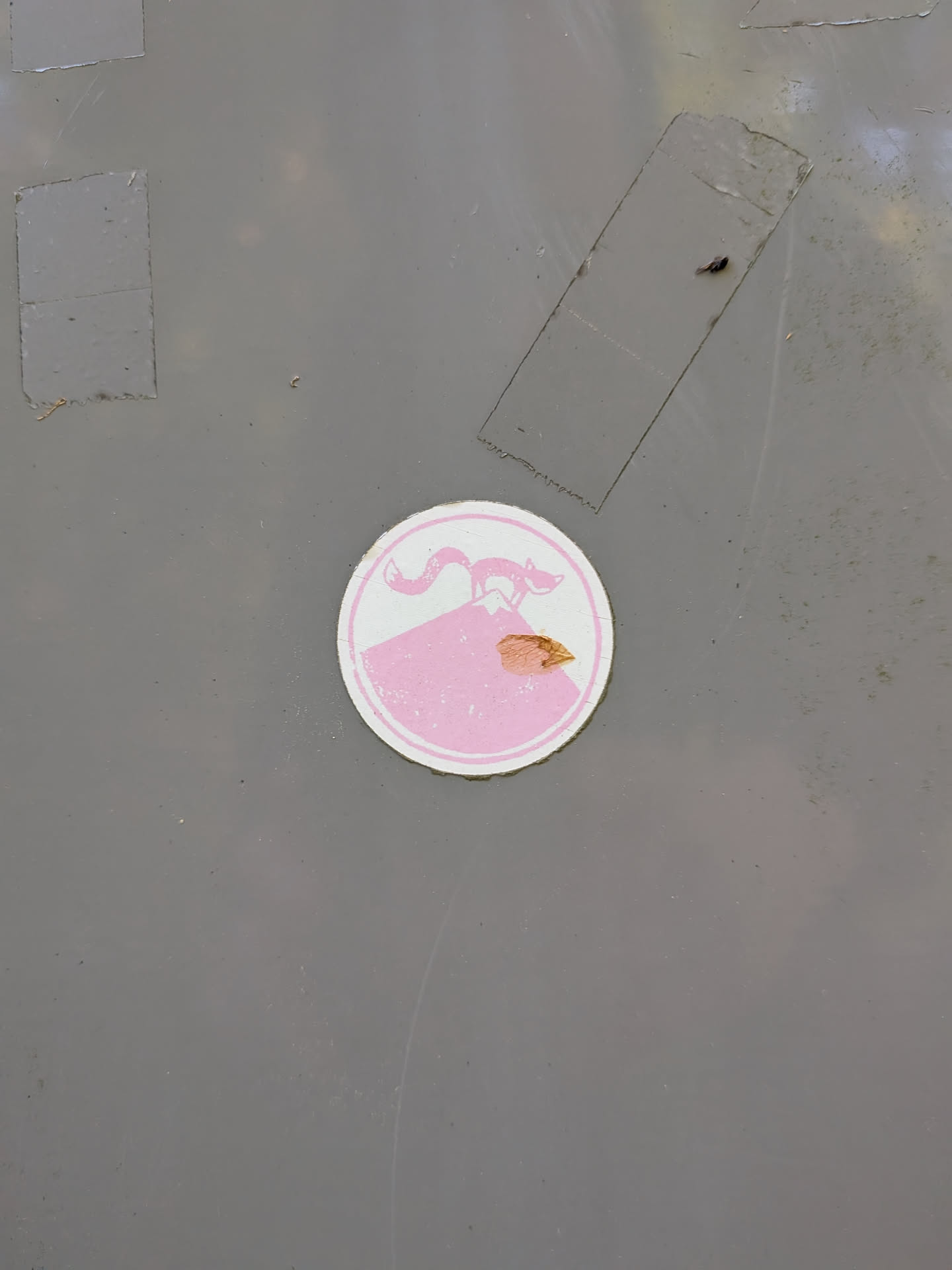 A circular pink and white sticker showing a stylized fox standing atop a mountain peak. It features a double-ring border and shows slight wear and a small tear.