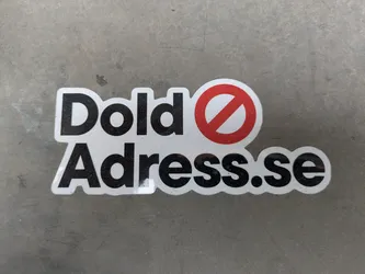 Street sticker The sticker is white with black text that reads "Dold Adress.se". There is a red circle with a line through it, replacing the letter 'O' in 'Dold'. The background is gray.