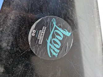 Street sticker A circular sticker with a dark grey background. The prominent feature is a large, stylized 'Loop' logo in a vibrant light blue/teal color, positioned on the right side with a registered trademark symbol. On the left side, stacked vertically in white sans-serif text, it reads 'PRO WRITING TOOLS' followed by 'MADE IN ITALY'. Below this text, there are two white social media icons: Facebook and Instagram. The sticker appears slightly worn and wrinkled, applied to a heavily scratched, dark surface.