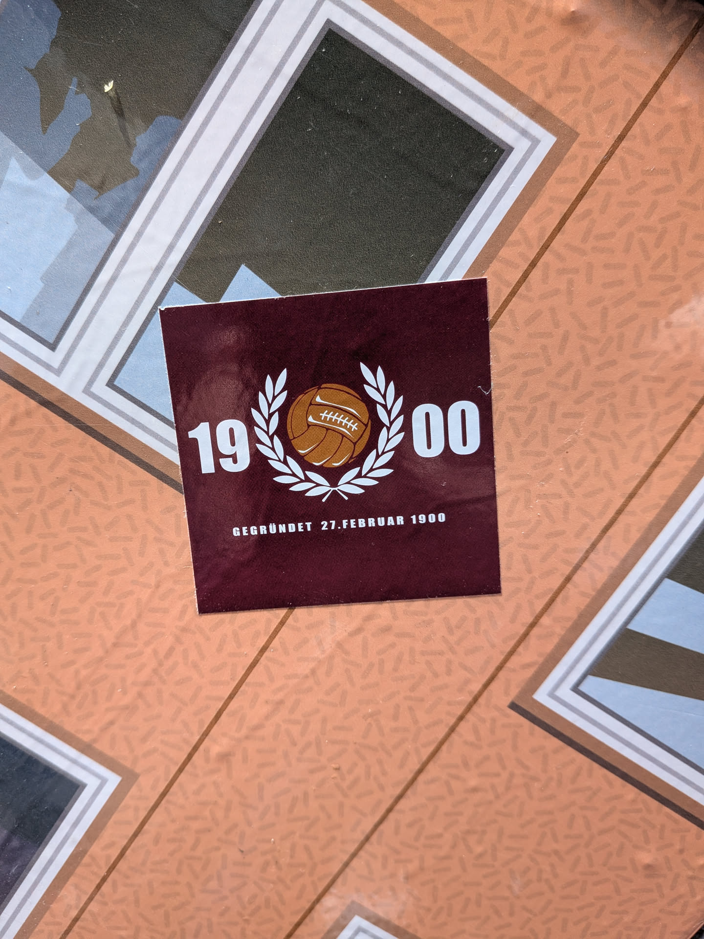 A square maroon sticker featuring a classic brown leather football enclosed in a white laurel wreath. The year '1900' is split on either side in white bold font, with the German text 'GEGRÜNDET 27.FEBRUAR 1900' printed below.