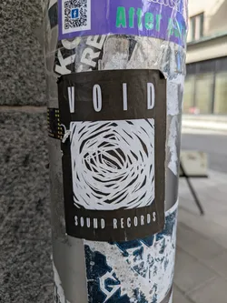 Street sticker The sticker is a black rectangle with the word "VOID" at the top and "SOUND RECORDS" at the bottom, both in white capital letters. In the center is a white, abstract drawing that resembles a vortex or a maze of intertwined lines.