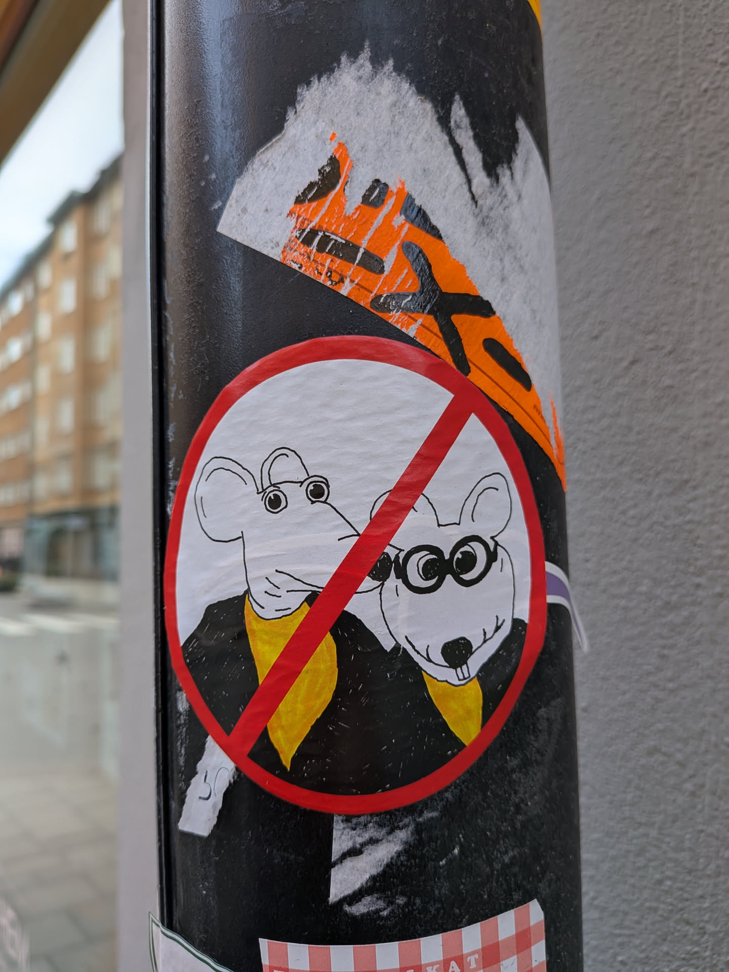 A circular sticker featuring a red prohibition symbol (a circle with a diagonal line) over two cartoon mice. Both mice are white with black outlines, wearing black jackets or suits and yellow scarves or ties. The mouse on the right wears round black glasses and has prominent front teeth. The background within the red circle is white. The sticker has a hand-drawn, somewhat whimsical style.