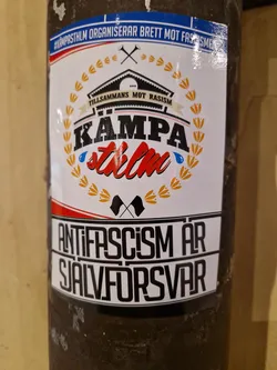 En dekal med budskapet "Tillsammans mot rasism" och texten "Kämpa, Stockholm".  Dekalen innehåller även texten "Antifascism är självförsvar".