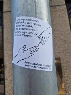 Street sticker A sticker with a drawing of two hands and a text in Polish. The text says that it takes a whole village to raise a child, but only one aunt to terminate a pregnancy. It also contains a website address.