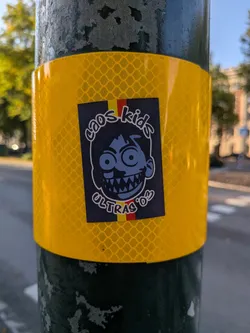 Street sticker Rectangular sticker on a yellow reflective band. Features a manic, wide-eyed blue cartoon face with sharp teeth. A vertical yellow and red stripe sits behind the character. Text reads 'caos kids' above and 'ULTRAS '03' below in white stylized font.