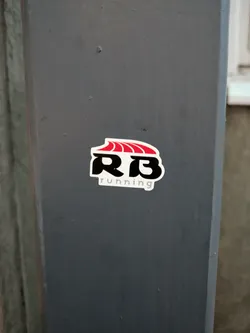 Street sticker A sticker featuring the RB Running logo, which includes stylized letters RB with a red wave-like design above them. The text "running" is present beneath the logo.