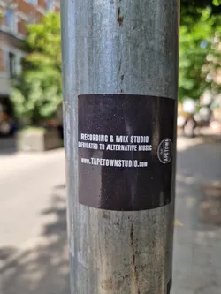 Street sticker A dark-colored sticker advertising Tapetown Studio, a recording and mix studio dedicated to alternative music. The sticker features the studio's website address and logo.