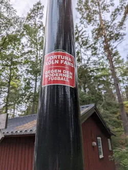 A rectangular red sticker with a thin white border, affixed to a black pole. It features bold white sans-serif text in German.