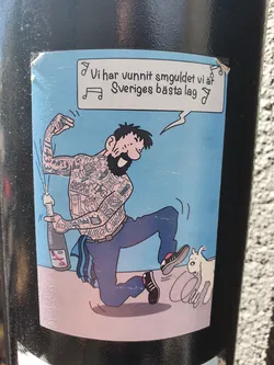 Street sticker A sticker featuring a cartoon illustration of a heavily tattooed man celebrating with a bottle of champagne. A small dog is shown running away from him. The text on the sticker translates to: "We have won the gold, we are Sweden's best team."