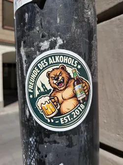 Street sticker Circular sticker with a dark green border. Features an aggressive brown bear holding a foaming beer mug and an Appenzeller beer bottle. Includes a silhouette of church towers and German text.