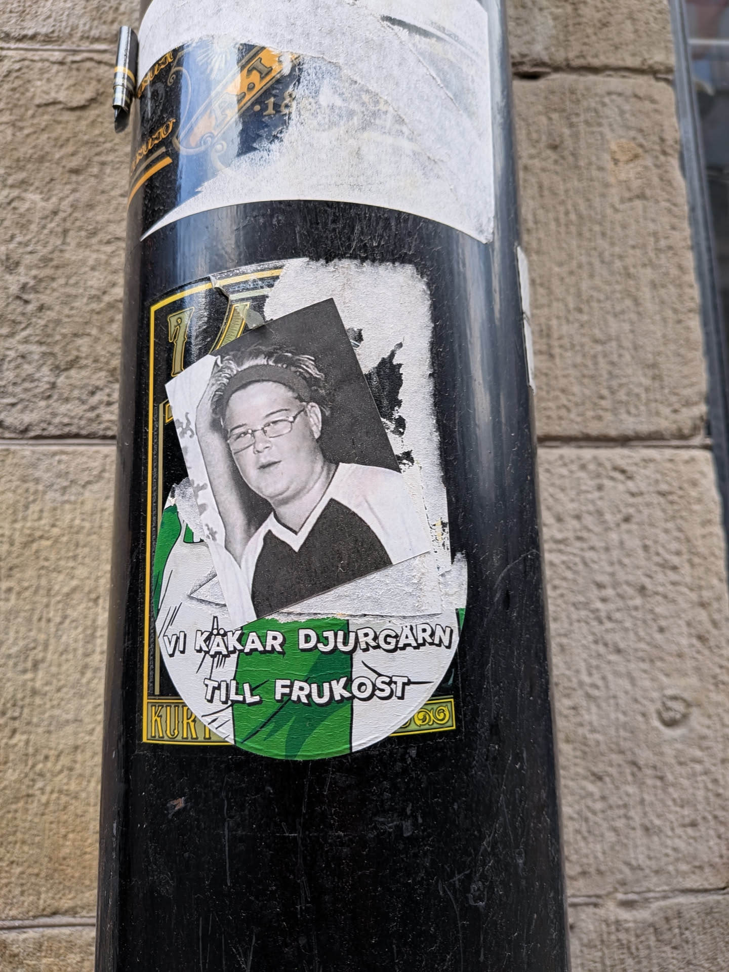 Circular sticker with green and white stripes. Features a black-and-white photo of a person with glasses and a headband. Swedish text 'VI KÄKAR DJURGÅRN TILL FRUKOST' is printed at the bottom.