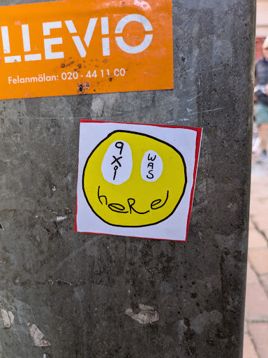 A square sticker featuring a yellow smiley face with a red border. Instead of eyes, the sticker has '9x1' and 'was' written in black. The word 'here' is written below the mouth.