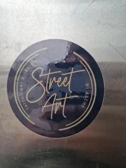 Street sticker Round sticker with a dark blue background and gold circular border. The text "Street Art" is written in a stylized script font in the center.  The smaller text around the circle says "Tattoo Art & Design by Asche".