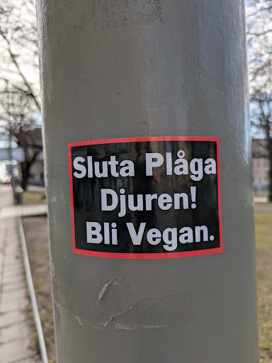 Street sticker The sticker features a black background with white text, surrounded by a red border. It reads "Sluta Plåga Djuren! Bli Vegan.", which translates to "Stop Torturing Animals! Go Vegan."