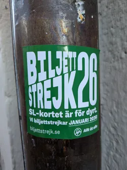 Street sticker A rectangular sticker with a vibrant green background and bold white text. The prominent headline reads 'BILJETTSTREJK26'. Below this, smaller white text states 'SL-kortet är för dyrt. Vi biljettstrejkar JANUARI 2026!'. At the bottom, a website address 'biljettstrejk.se' is displayed alongside a circular logo featuring a stylized 'A' and the phrase 'Allt åt alla'. The sticker is affixed to a dark, weathered, cylindrical pole.