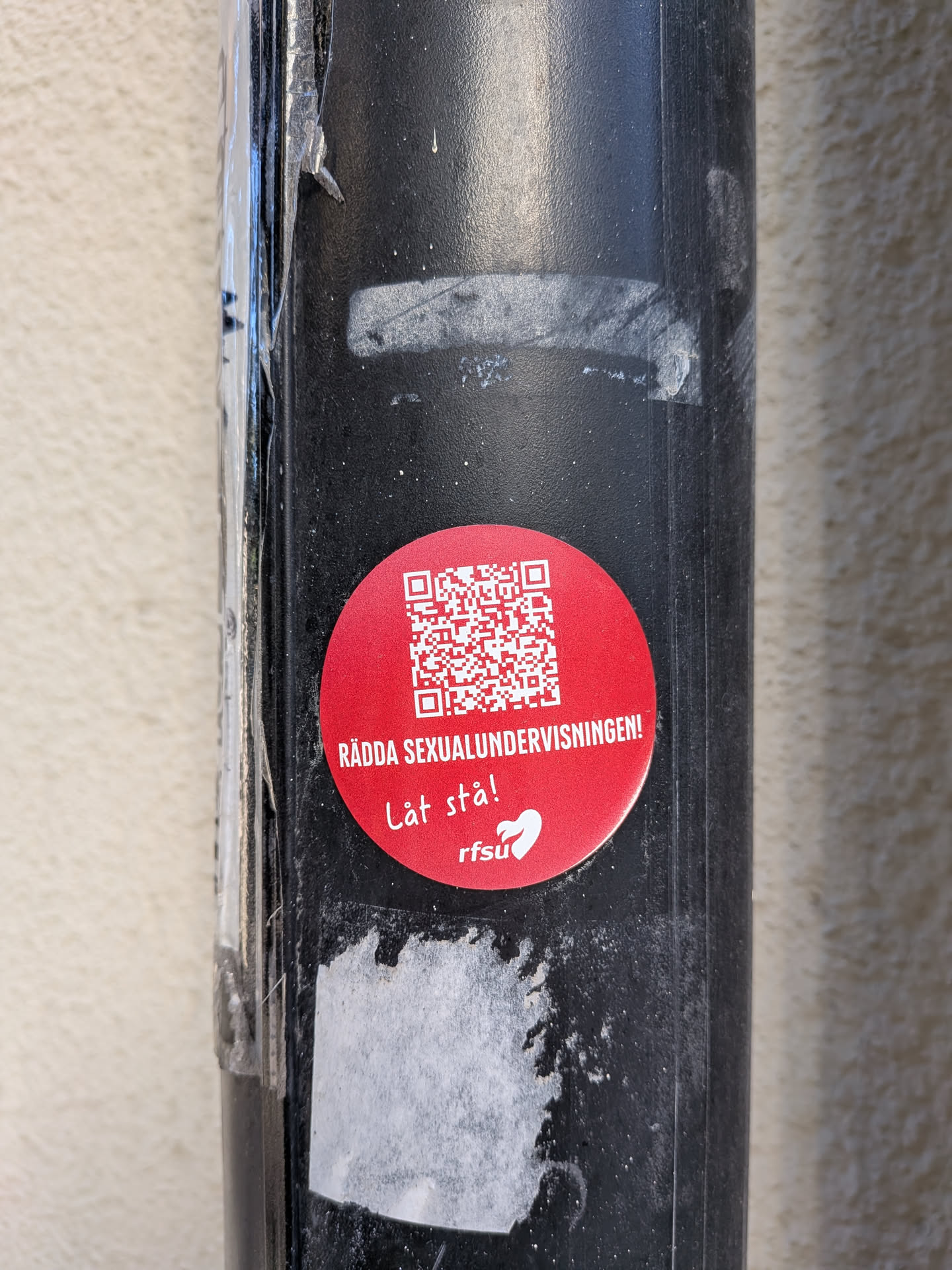 A circular red sticker with a QR code prominently displayed in the upper half. Below the QR code, in white text, are the phrases "RÄDDA SEXUALUNDERVISNINGEN!" and "Låt stå!". At the bottom of the sticker, the abbreviation "rfsu" is visible alongside a stylized white heart shape.