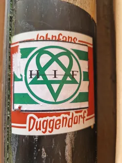 Street sticker A sticker featuring the logo of H.I.F. Duggendorf, a possible band or club. The logo is a green intertwined heart shape with the letters H.I.F inside. The sticker has a red and white border with the text "Johnfans" at the top and "Duggendorf" at the bottom.