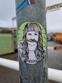 Street sticker A round sticker featuring a stylized illustration of a person with long hair and a mustache, holding scissors. The text on the sticker says "BackBarberStop".