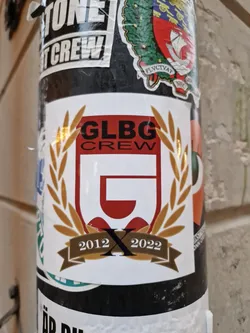 A sticker commemorating the 10th anniversary of GLBG Crew (2012-2022). The design features a crest with the crew's logo,  flanked by laurel wreaths and a banner displaying the years. 