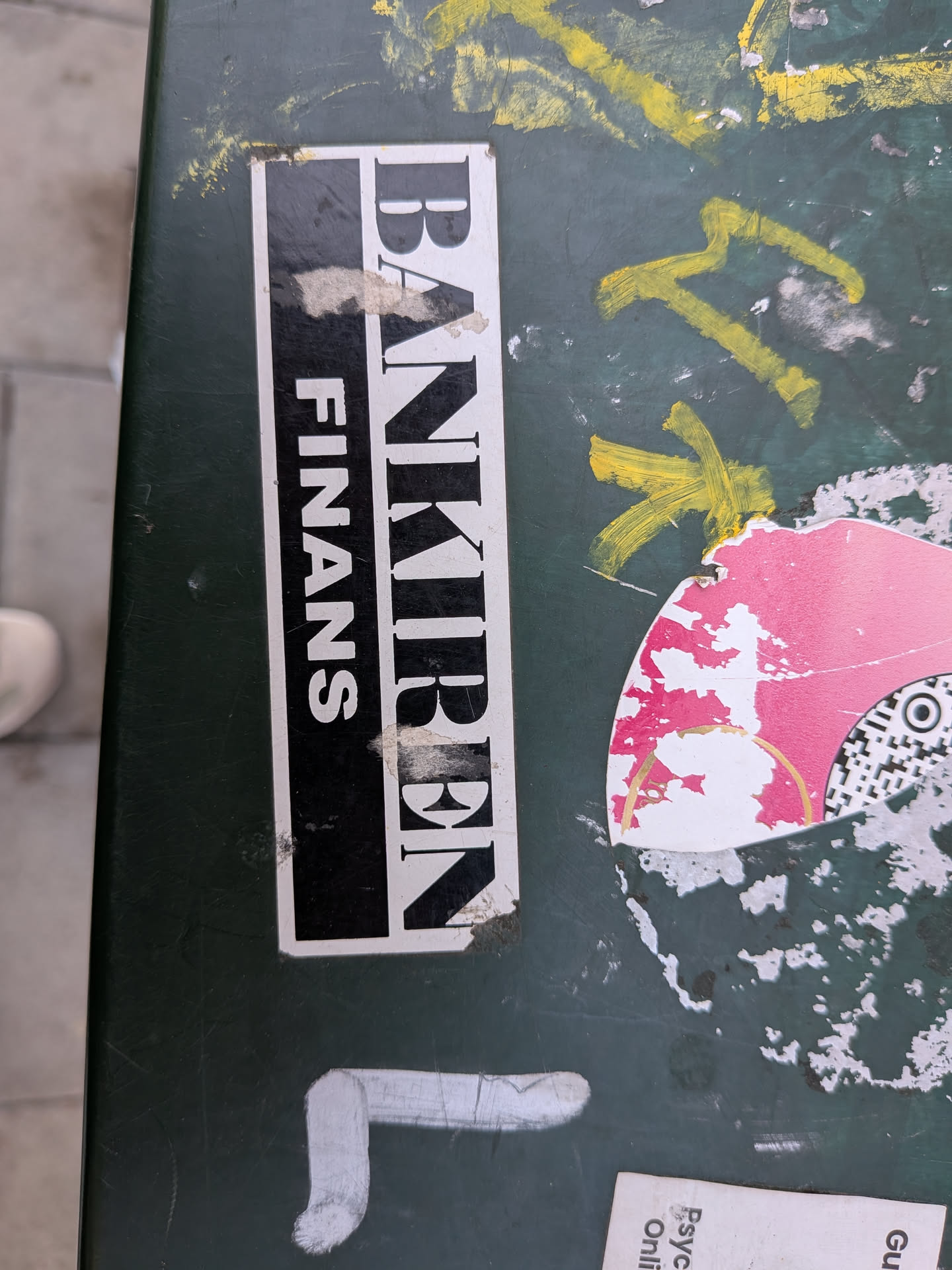 A rectangular sticker split vertically. The left side is black with white sans-serif text 'FINANS'. The right side is white with black serif text 'BANKIREN'. It is stuck to a green surface and shows slight wear.