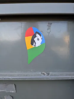 Street sticker The sticker is shaped like the iconic Google Chrome logo pin, featuring its characteristic four-color segments: red in the top-left, yellow in the bottom-left, green in the bottom-right, and blue in the top-right. Superimposed over the center of these colors is a black and white portrait of a man, strongly resembling philosopher Friedrich Nietzsche, with a prominent mustache and a serious expression. The portrait is slightly off-center, with his face primarily covering parts of the yellow, blue, and red sections. The sticker has a clean, die-cut edge and is adhered to a textured, grey metallic surface.