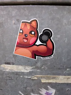 Street sticker The sticker depicts a stylized, anthropomorphic cat with large, expressive eyes and rosy cheeks. The cat has orange and brown fur with darker stripes on its head and ears. It is shown from the chest up, flexing a muscular arm that is holding a black dumbbell. The background of the sticker is white, with a thin black outline around the cat and its accessories. Below the cat's arm, the text 'twitch.tv/melou' is visible in a small, white font on a black background.