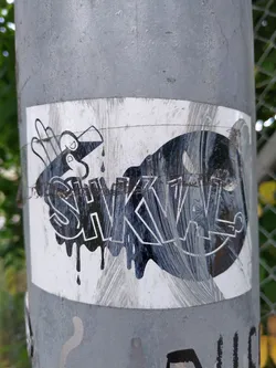 Black and white sticker with the text SKWL in a dripping style.  It features a hand-like figure pouring liquid. The sticker shows some wear and tear.