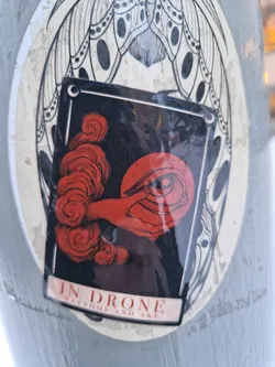 Street sticker A sticker featuring an illustration of a hand emerging from red clouds, holding an eye.  The style is dark and evocative, with fine line details. The sticker is affixed to a larger sticker with a moth-like design.