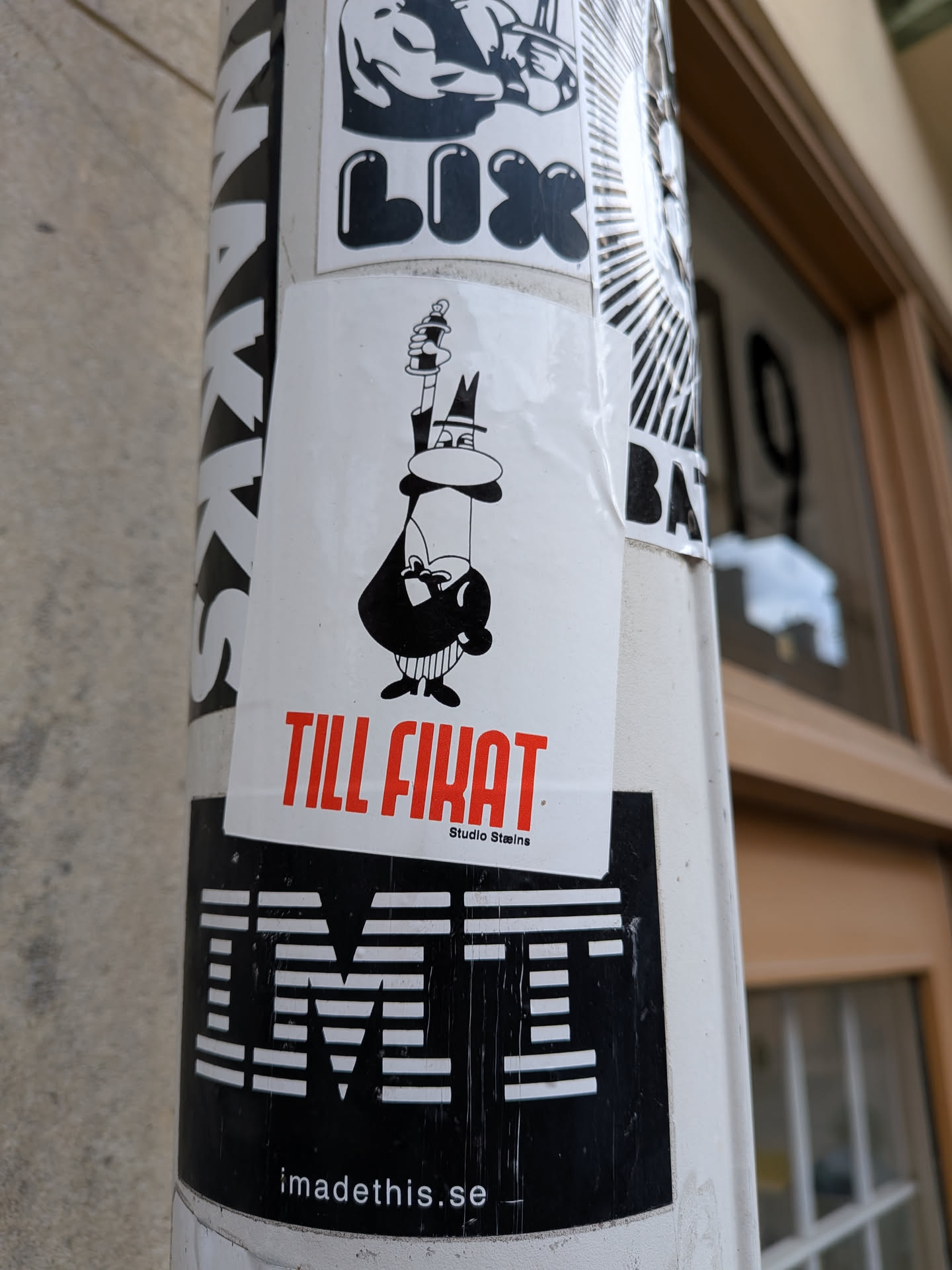 The sticker features a whimsical, black and white cartoon character on a white rectangular background. The character, depicted in a minimalist style, wears a top hat and a suit, has a prominent nose, and a small beard. It holds a spray paint can upright like a scepter or staff. Below the character, in large red capital letters, is the text 'TILL FIKAT', with 'Studio Stains' written in smaller black text underneath. The overall aesthetic is clean and graphic.