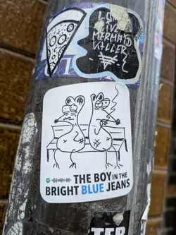 Street sticker The central sticker is a white, rectangular shape with rounded corners, featuring a black line-art drawing on a white background. It depicts two stylized, somewhat mouse-like or rat-like cartoon figures with large ears and prominent snouts, sitting side-by-side on a park bench. The figure on the right is smoking a cigarette, indicated by a small red tip and a wavy line representing smoke. Both figures have simple, somewhat dazed or relaxed expressions. Below the drawing, there's a small green Spotify logo followed by a black sound wave graphic. Underneath this, the text "THE BOY IN THE BRIGHT BLUE JEANS" is written in black, with the word "BLUE" highlighted in a vibrant blue color. The overall style is whimsical and minimalist.