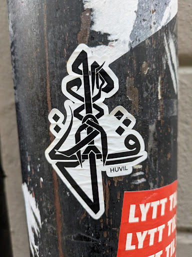 A black and white abstract sticker featuring a unique design with the artist's signature, HUVIL, subtly placed on the sticker. The style is minimalist and geometric, with sharp lines and shapes creating a visually striking image. It's stuck on a dark, textured surface, adding a gritty urban vibe. 