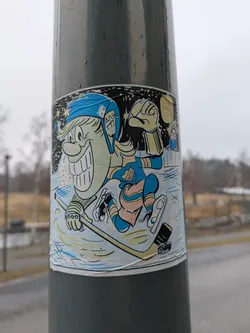 Street sticker A sticker featuring a cartoon hockey player with a wide grin and a blue helmet, skating on ice. The player is wearing a blue and yellow uniform and holding a hockey stick.